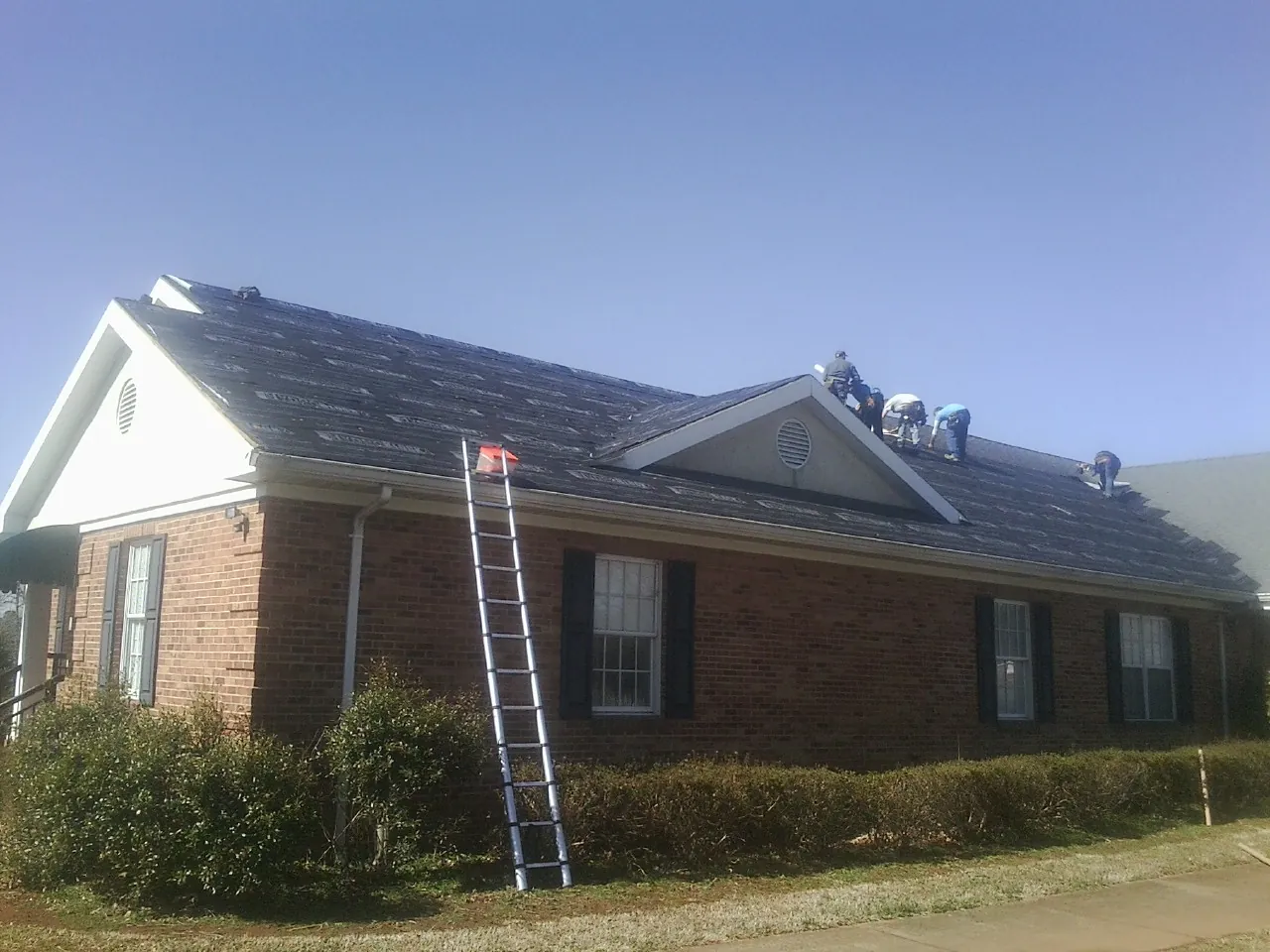 Crew tearing shingles off a brick ranch roof with a ladder set — Metal Roof Repair work by our crew in Essex