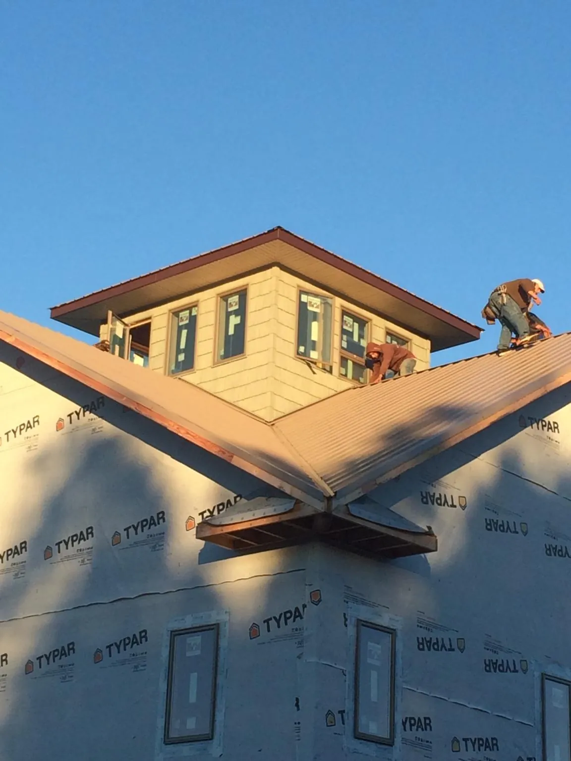 Roofers working around a rooftop cupola on a new metal roof at sunset — Roof Waterproofing in Essex by Roofing Brothers